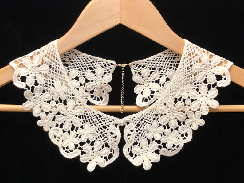 May include: White lace collar with a delicate floral pattern. The collar has a chain attached to the back for fastening.
