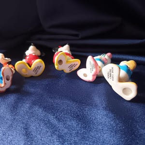 May include: Five small Disney figurines, including Mickey Mouse, Donald Duck, and Minnie Mouse, are arranged on a blue surface. The figurines are made of bone china and are in various poses, with their undersides visible.