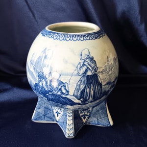 May include: A blue and white ceramic vase with a star-shaped base and a scene of people in traditional clothing. The vase is decorated with a blue and white pattern.