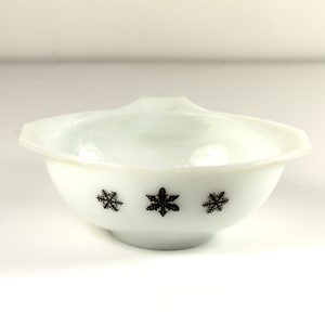 May include: White ceramic bowl with a black snowflake design. The bowl has a handle on one side.