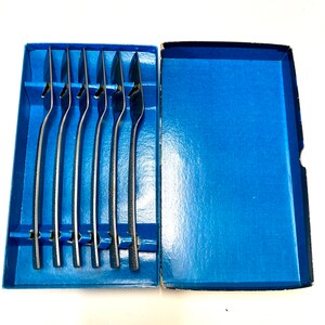 Puede incluir: Un juego de seis piezas de cubiertos plateados en una caja azul. Los cubiertos están dispuestos en una fila, con los mangos hacia arriba. La caja está hecha de cartón y tiene un forro azul.