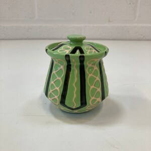 May include: A small green ceramic jar with a lid. The jar has a geometric pattern of black and white lines.