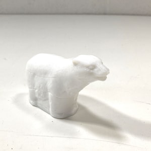May include: A small, white polar bear figurine. The bear is sculpted with visible details, including its head, body, and legs. The figurine is made of a solid, opaque white material and has a smooth finish. The bear is standing upright.