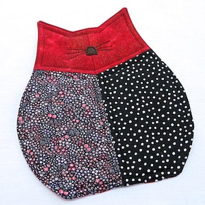 Può includere: Un sottopentola a forma di gatto rosso e nero con un motivo floreale su un lato e un motivo a pois sull'altro.