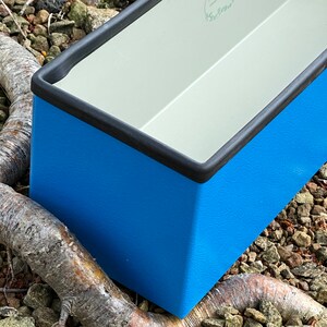 May include: A blue rectangular planter with a black rim. The planter is made of a textured material and has a white interior.