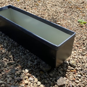 May include: A black rectangular planter with a light grey interior. The planter is made of metal and has a slightly rounded edge.