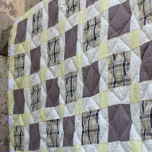 Peut inclure: Une courtepointe patchwork avec un motif à carreaux dans les tons de brun, jaune et blanc. La courtepointe est faite de différents tissus et est matelassée avec un motif en losange.