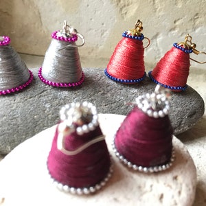 Peut inclure: Un ensemble de six boucles d'oreilles faites à la main en forme de cône avec une bordure perlée. Les boucles d'oreilles sont disponibles en trois couleurs : argent, rouge et bordeaux.