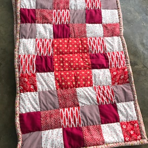 Peut inclure: Une courtepointe rouge et blanche en patchwork avec une variété de motifs, y compris des étoiles, des pois et des motifs géométriques.