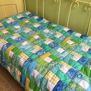 Peut inclure: Une courtepointe en patchwork avec une variété de tissus verts, bleus et blancs. La courtepointe est composée de carrés et de rectangles, et les motifs des tissus sont floraux, paisley et à pois.