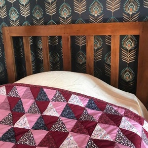 May include: A wooden headboard with patterned wallpaper behind it. A pink and burgundy quilt is on the bed.