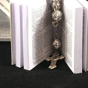 May include: A small white book with a silver cross charm and a silver rosary attached to it.