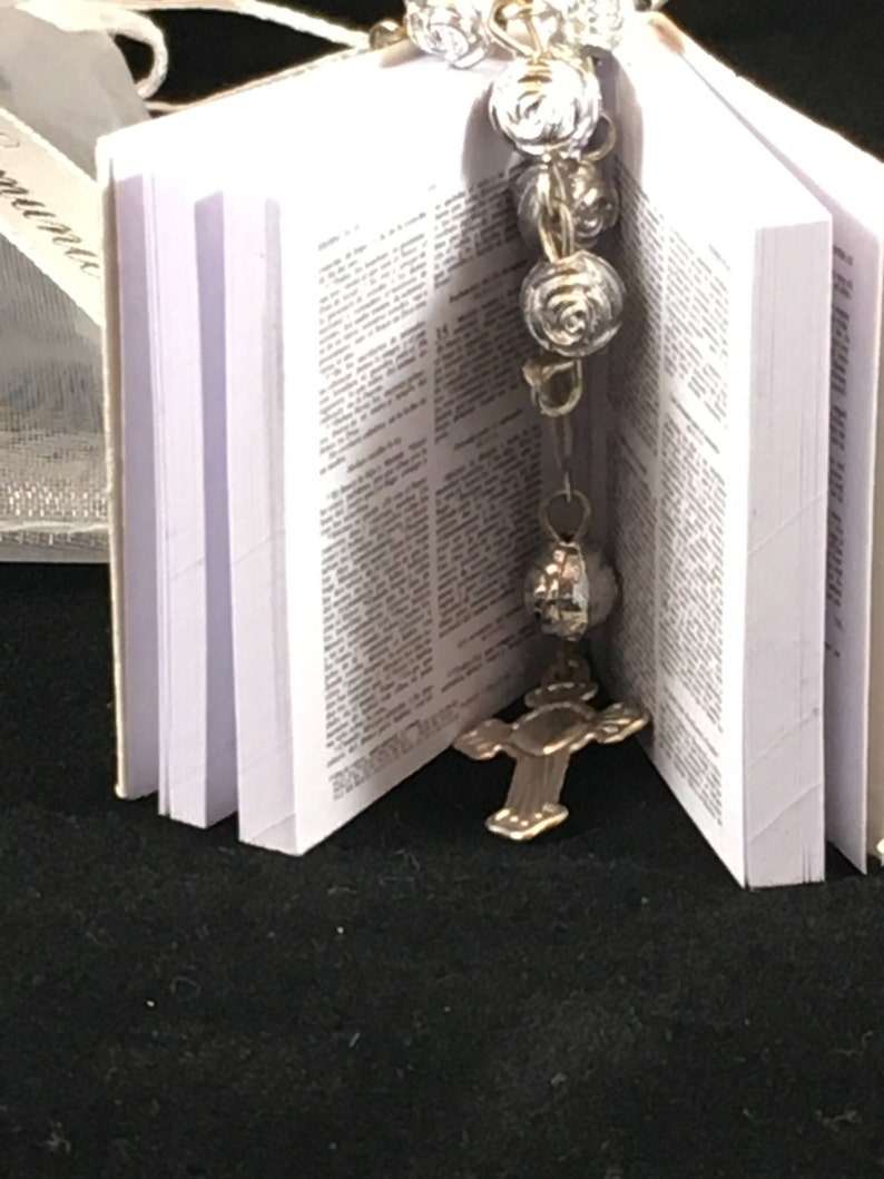 May include: A small white book with a silver cross charm and a silver rosary attached to it.
