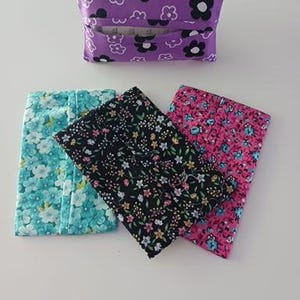 May include: Four rectangular fabric tissue holders featuring various floral patterns. One holder is purple with white and black flowers, while the others display teal, black, and pink backgrounds with intricate multi-colored floral prints.