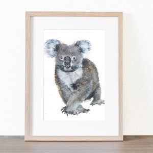 May include: Watercolor painting of a koala bear in a wooden frame. The koala is depicted in shades of gray and brown, with a white chest and fluffy ears. The artwork is set against a white background.
