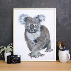 May include: A framed watercolor painting of a koala bear in shades of gray, white, and brown. The koala is depicted with detailed fur and expressive eyes. The artwork is displayed with a gold frame.
