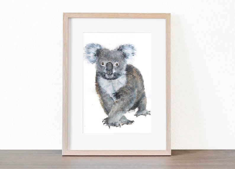 May include: Watercolor painting of a koala bear in a wooden frame. The koala is depicted in shades of gray and brown, with a white chest and fluffy ears. The artwork is set against a white background.