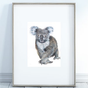 May include: Watercolor painting of a koala bear in a wooden frame. The koala is depicted in shades of gray and brown, with a fluffy appearance. The artwork is set against a white background, creating a clean and simple aesthetic.