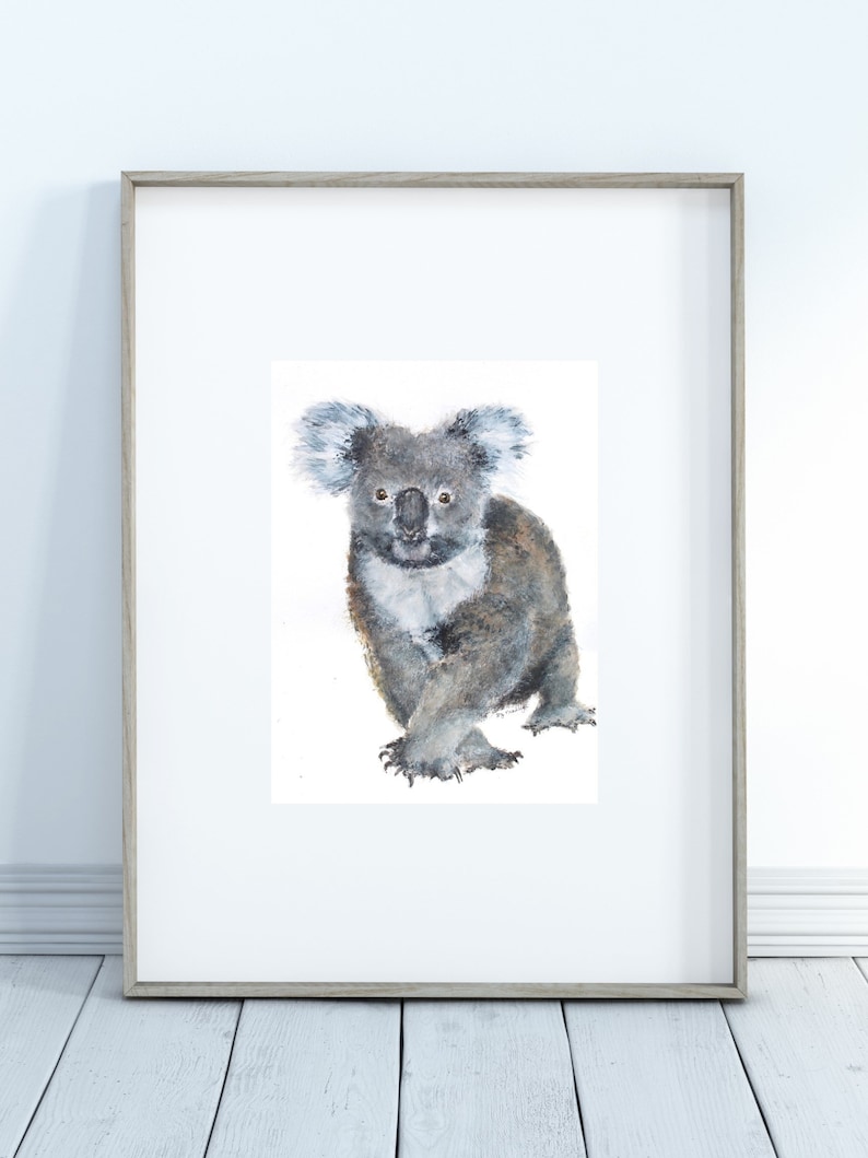 May include: Watercolor painting of a koala bear in a wooden frame. The koala is depicted in shades of gray and brown, with a fluffy appearance. The artwork is set against a white background, creating a clean and simple aesthetic.
