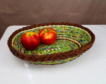 Puede incluir: Una cesta tejida con un patrón verde, blanco y marrón, llena de dos manzanas rojas.