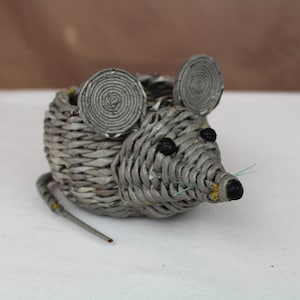 Könnte beinhalten: Ein grauer, geflochtener, mausförmiger Pflanztopf mit schwarzen Augen und einem grünen Schwanz.