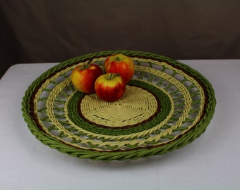 Puede incluir: Una cesta tejida con un patrón verde, marrón y crema, que contiene tres manzanas rojas y amarillas.