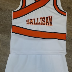May include: White cheerleading uniform with orange and black trim. The top has a V-neck and the skirt is pleated. The word "SALLISAW" is embroidered on the top.