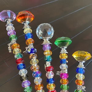 May include: Six colorful beaded wands with crystal tops. The wands are made with various colored beads and charms. The crystal tops are in shades of purple, orange, clear, green, and yellow.