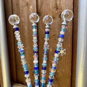 May include: Four decorative garden stakes with crystal ball tops and blue and white beads. The stakes have a snowflake charm at the bottom. The text "Price per stake" is visible at the top of the image.