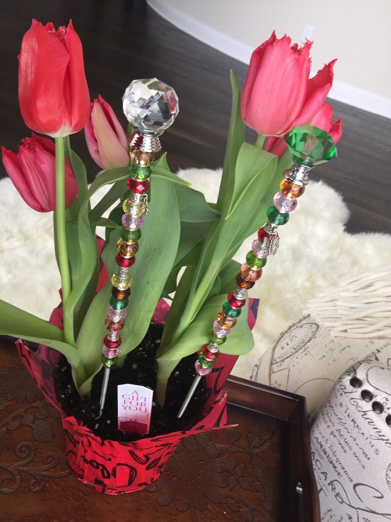 May include: A potted plant with red tulips and two decorative sticks with colorful beads and crystal accents. The plant pot is red with a white label that says "A Gift For You".
