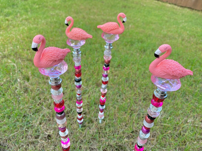 Pode incluir: Quatro estacas de jardim de flamingo rosa com contas de cristal e contas rosa, vermelhas e pretas. As estacas s&atilde;o de metal e t&ecirc;m um acabamento prateado.