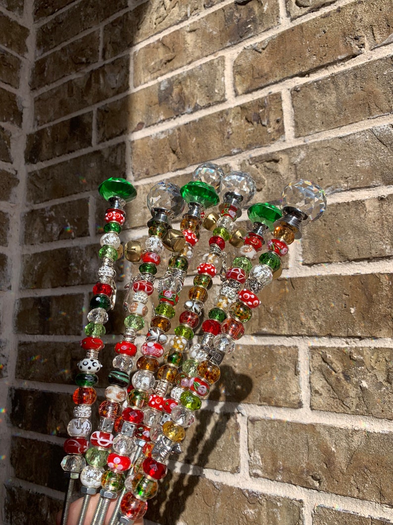 May include: A set of seven beaded wands with crystal tops. The beads are red, green, white, and gold. The wands are made of metal and have a silver finish.