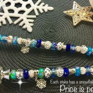May include: Two silver snowflake themed stakes with crystal glass tops and blue and white beads. Each stake has a snowflake charm. "Price is per stake."