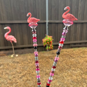Pode incluir: Duas estacas de jardim de flamingo rosa com caules de contas. As contas s&atilde;o rosa, vermelho, preto, prata e transparente. As estacas medem aproximadamente 60 cm de altura.