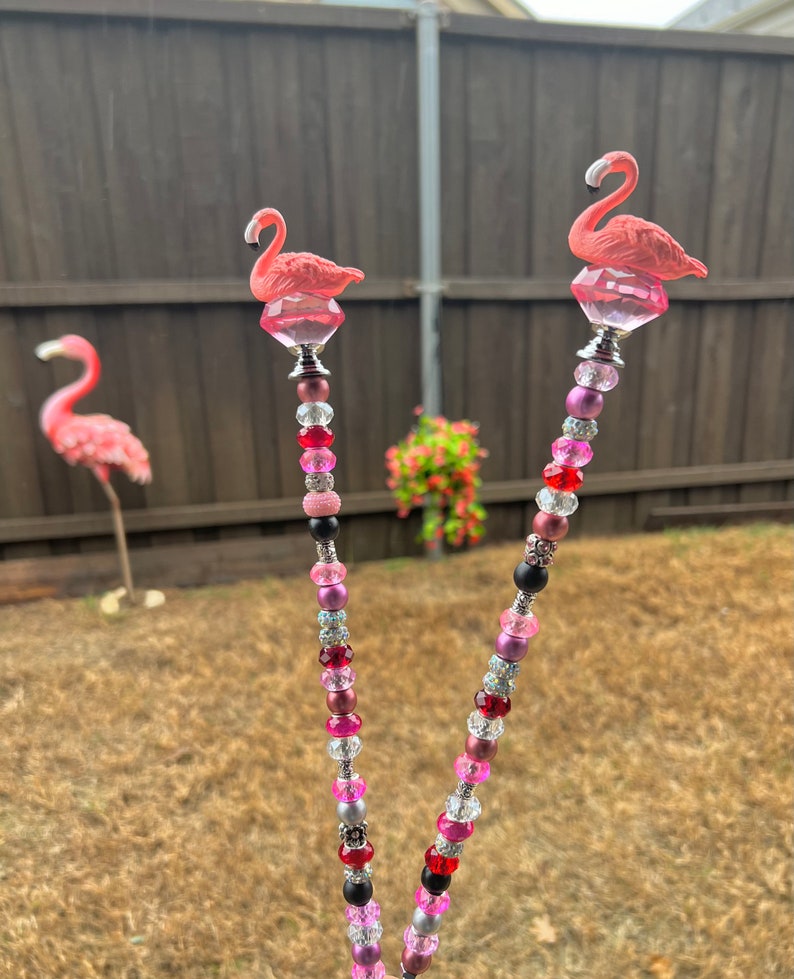 Pode incluir: Duas estacas de jardim de flamingo rosa com caules de contas. As contas s&atilde;o rosa, vermelho, preto, prata e transparente. As estacas medem aproximadamente 60 cm de altura.