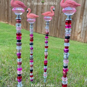 Pode incluir: Quatro estacas de jardim de flamingo rosa com topos de cristal e contas coloridas. As estacas s&atilde;o de metal e t&ecirc;m uma ponta afiada para f&aacute;cil inser&ccedil;&atilde;o no solo.  Idea, Design & Creation by Threads and Wicks. Pre&ccedil;o por estaca.
