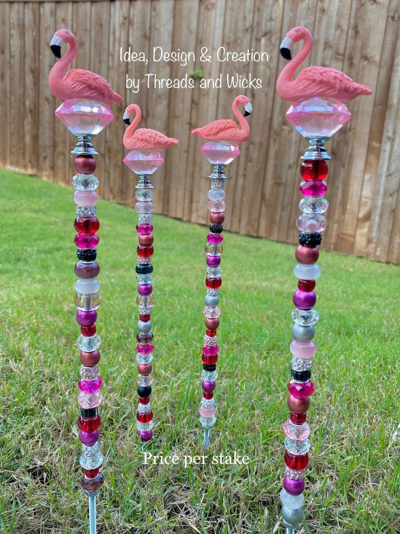 Pode incluir: Quatro estacas de jardim de flamingo rosa com topos de cristal e contas coloridas. As estacas s&atilde;o de metal e t&ecirc;m uma ponta afiada para f&aacute;cil inser&ccedil;&atilde;o no solo.  Idea, Design & Creation by Threads and Wicks. Pre&ccedil;o por estaca.