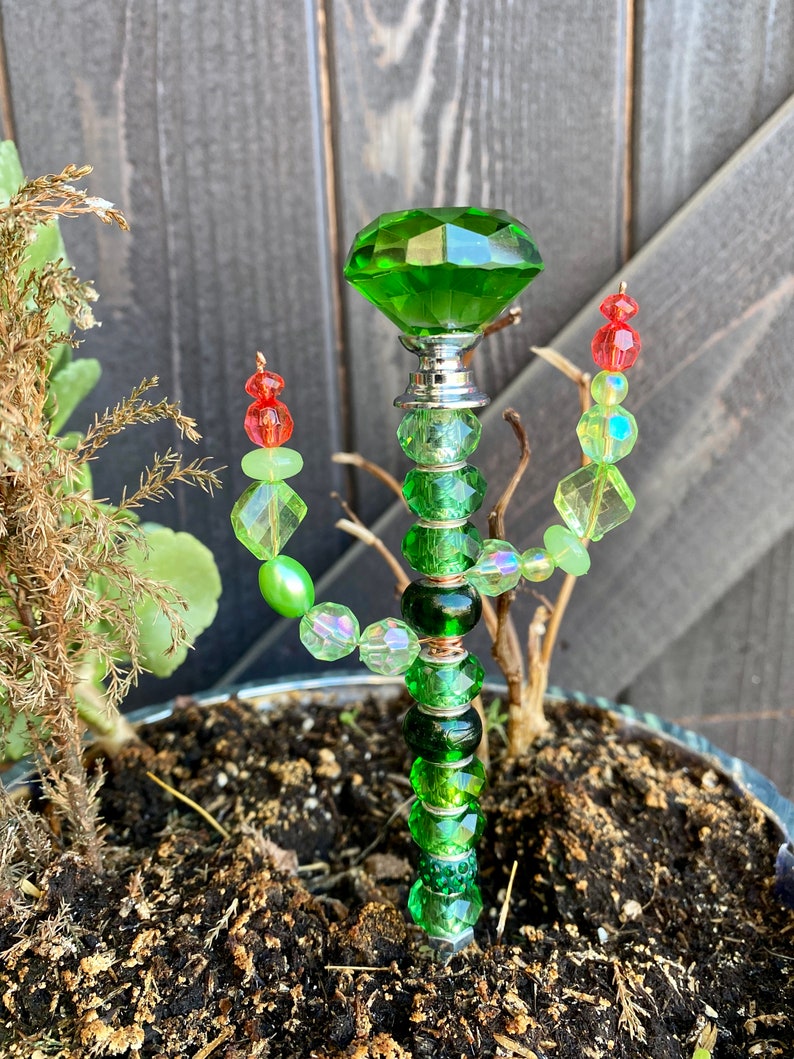 May include: A green glass cactus garden stake with a large green crystal on top and green, red, and iridescent beads.