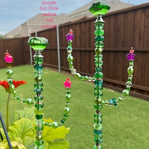 May include: Three green beaded cactus stakes with crystal toppers. The stakes are 1 foot tall and the beaded portion is 9 inches tall. The crystal toppers are available in purple, hot pink, yellow, red, or orange.