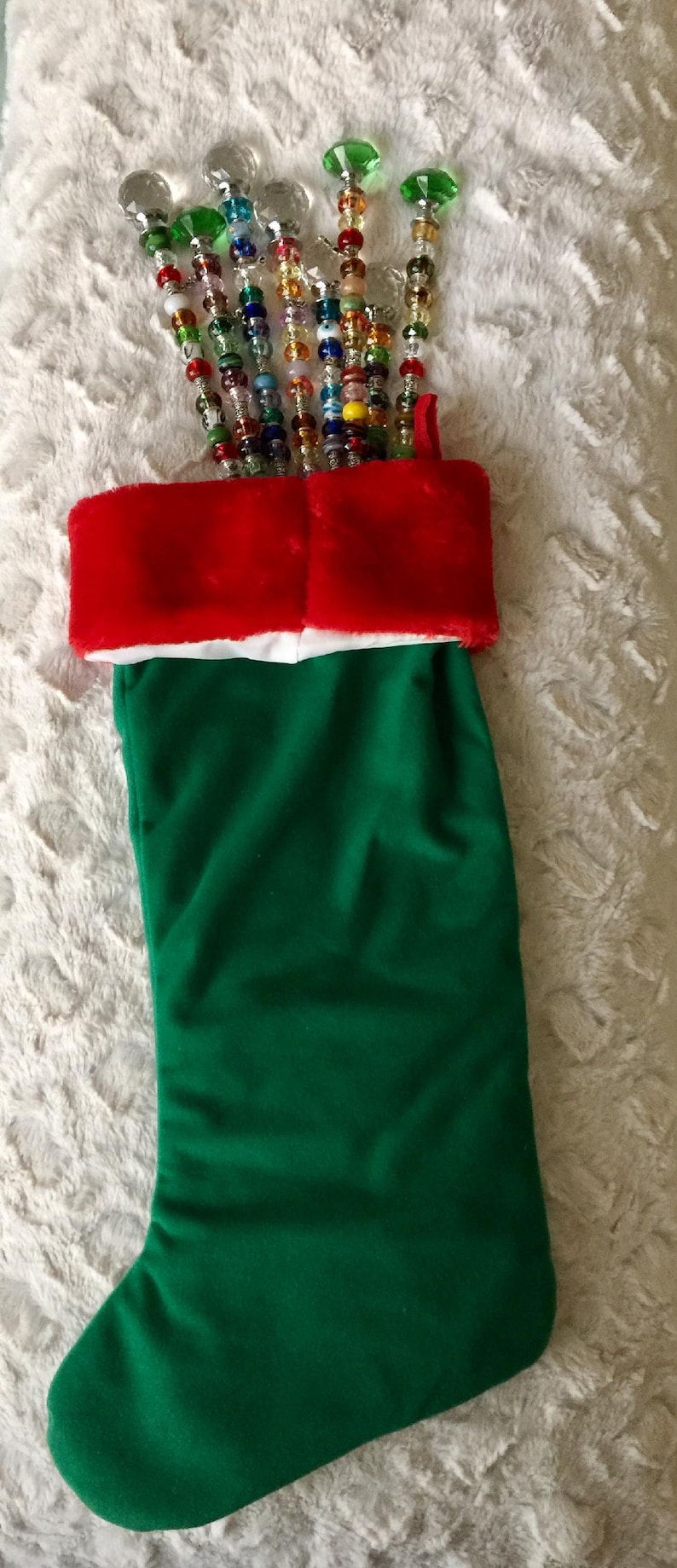 May include: A green Christmas stocking with a red and white cuff. The stocking is filled with colorful beaded wands with crystal tops.