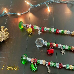 May include: Three Christmas tree toppers with red, green, and gold beads, bells, and charms. The toppers are made with a crystal, a clear glass ball, and a green gem.