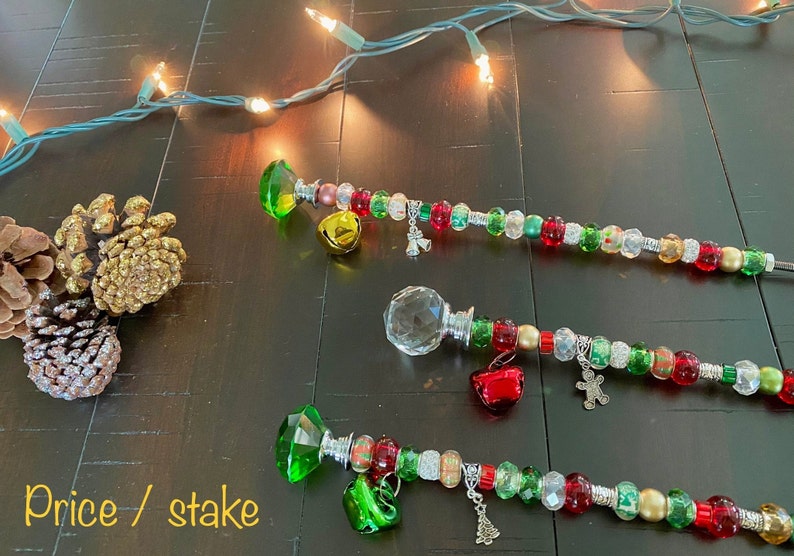 May include: Three Christmas tree toppers with red, green, and gold beads, bells, and charms. The toppers are made with a crystal, a clear glass ball, and a green gem.