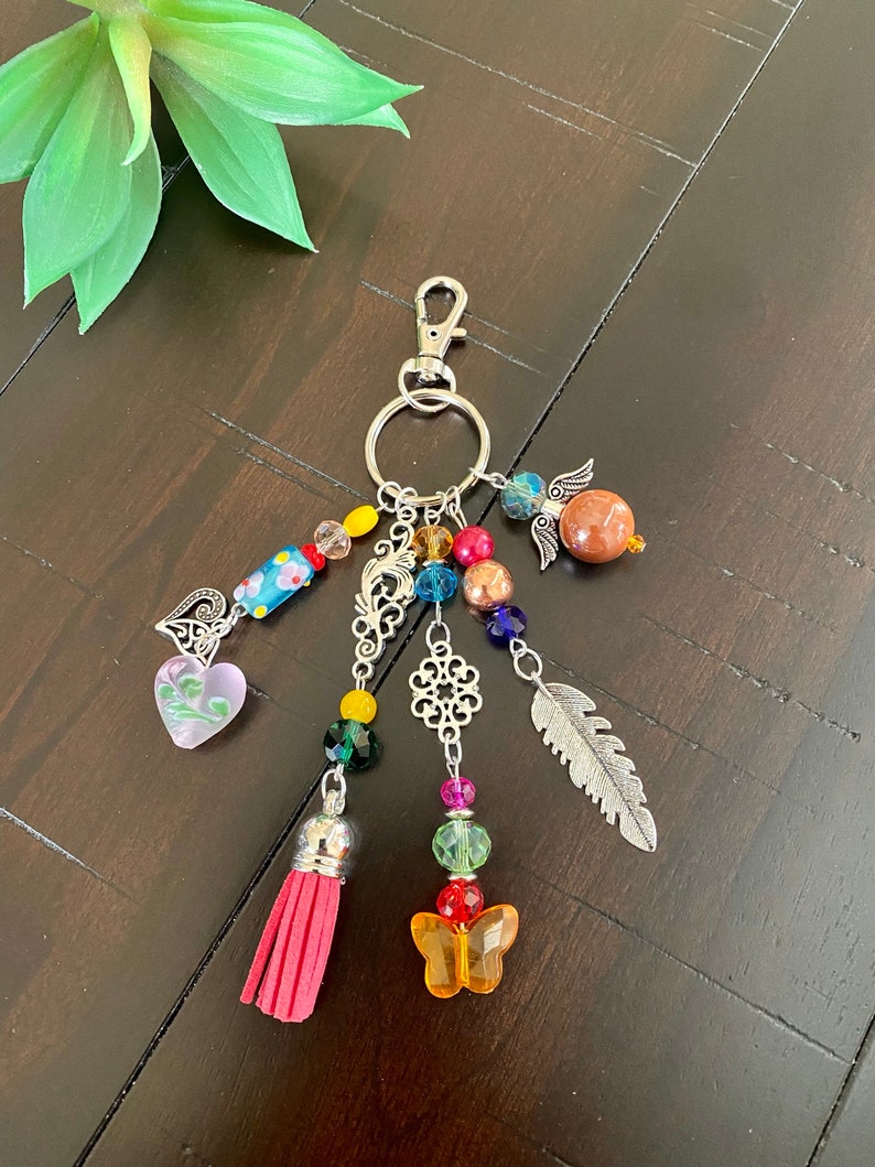 May include: A colourful keychain with a silver charm, beads, a pink heart, a feather, a butterfly, and a tassel.