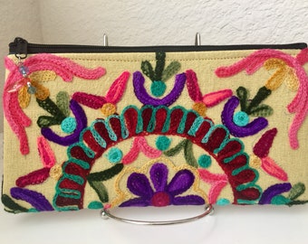 Può includere: Una pochette beige con cerniera con fiori e foglie ricamati colorati. La pochette ha un manico in metallo argentato.