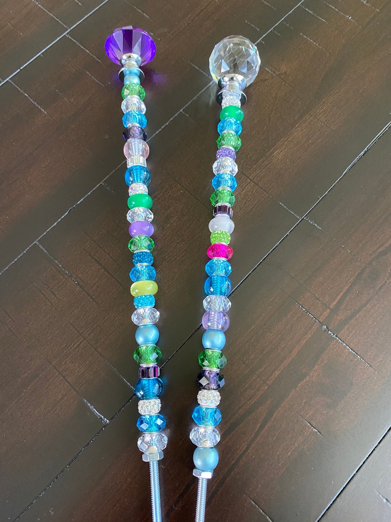 May include: Two decorative garden stakes with crystal tops and colorful beads. The stakes are made of metal and have a silver finish. The beads are in various colors, including blue, green, purple, and pink.