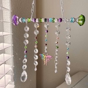 May include: A crystal suncatcher with a silver chain, featuring a butterfly charm and colorful beads. The suncatcher has multiple strands of clear crystal beads with a teardrop crystal at the end of each strand.