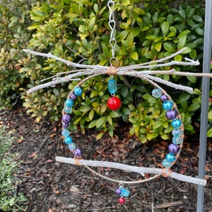 May include: A hanging mobile made of twigs, wire, and beads. The mobile features a circular frame with purple, blue, and turquoise beads, and red beads hanging from the bottom.