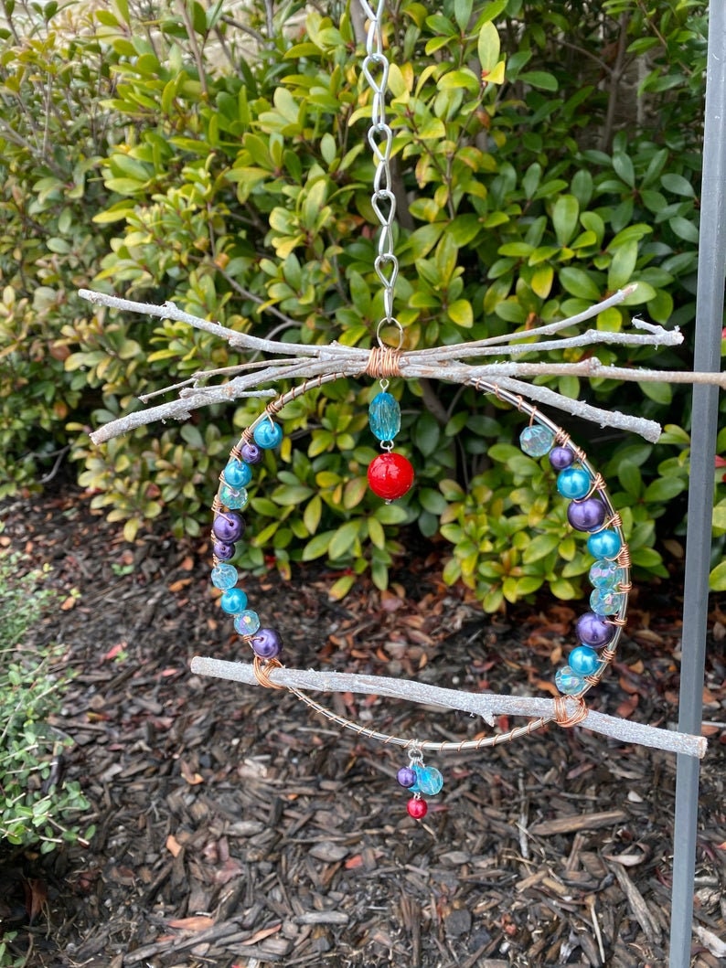 May include: A hanging mobile made of twigs, wire, and beads. The mobile features a circular frame with purple, blue, and turquoise beads, and red beads hanging from the bottom.
