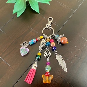 May include: A colourful beaded keychain with a silver charm, a pink heart, a feather, a butterfly, and a tassel.