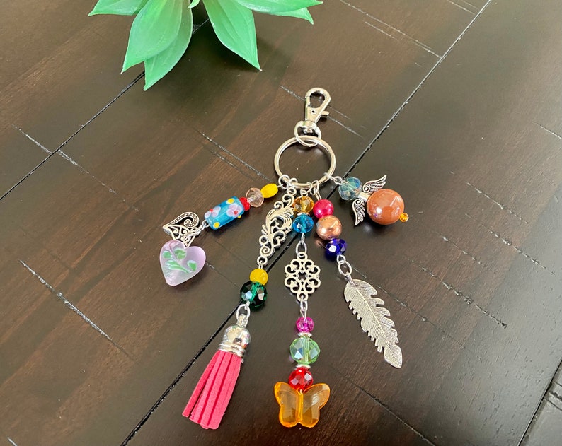 May include: A colourful beaded keychain with a silver charm, a pink heart, a feather, a butterfly, and a tassel.